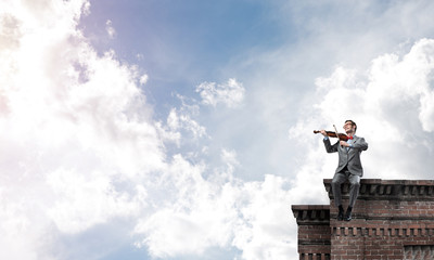 Handsome violinist in glasses on building edge play his melody