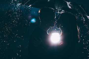 young couple standing under a dark umbrella