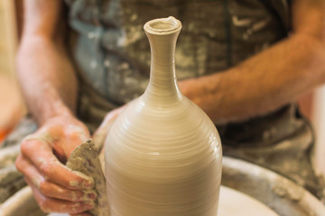 Potter creating a ceramics clay vase. Man sculptor in the workshop makes a jug out of earthenware closeup. Twisted potter's wheel. Hands detail. Small business concept.