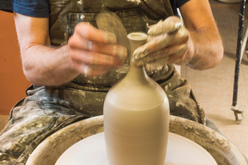 Potter creating a ceramics clay vase. Man sculptor in the workshop makes a jug out of earthenware closeup. Twisted potter's wheel. Hands detail. Small business concept.