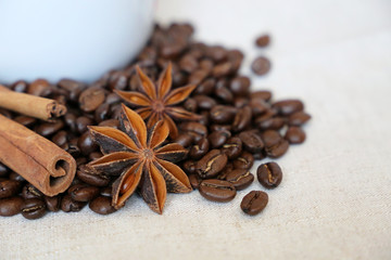 Coffee with spices. White cup, dark roasted coffee beans, cinnamon sticks and star anise on the burlap
