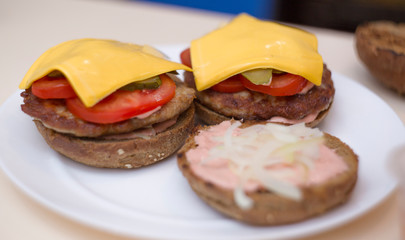 Preparing delicious burgers. Chef cooking meat burgers with bacon, cheese and vegetables, selective focus. Close-up.