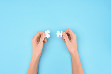 cropped shot of woman holding white puzzles pieces on blue background