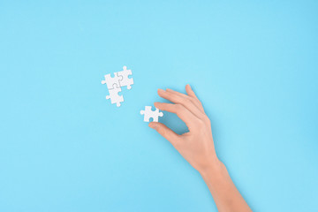 partial view of woman with white puzzles pieces on blue background