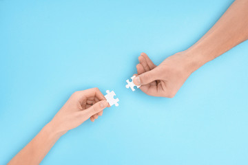 cropped shot of man and woman with white puzzle pieces on blue backdrop, cooperation concept