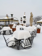 Tables and chairs from a terrace under the snow with clock tower in the background
