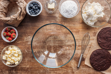 top view of empty glass bowl, whisk and ingredients for delicious homemade cake on wooden table