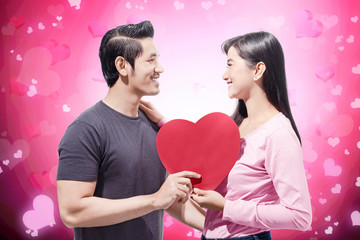 Fototapeta na wymiar Young asian couple holding red heart shape and looking at one another