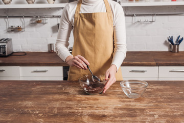 mid section of woman in apron mixing ingredients and preparing gourmet sweet cake