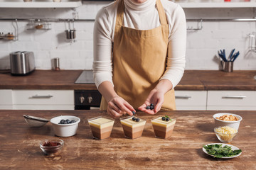 mid section of woman in apron preparing triple chocolate mousse in glasses