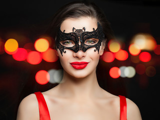 Young smiling woman in sexy carnival mask on abstract red night glitter bokeh background