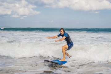 Young man, beginner Surfer learns to surf on a sea foam on the Bali island