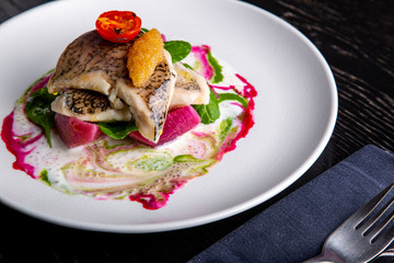 delicious restaurant dish of white fish, pike, sea bass with vegetables under the sauce in restaurant background. Healthy exclusive food on big white plate closeup
