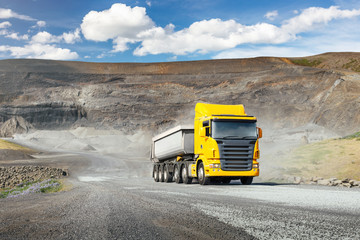Modern yellow truck with white heavy duty dump trailer drives after load from quarry in a sunny day
