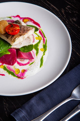 delicious restaurant dish of white fish, pike, sea bass with vegetables under the sauce in restaurant background. Healthy exclusive food on big white plate closeup