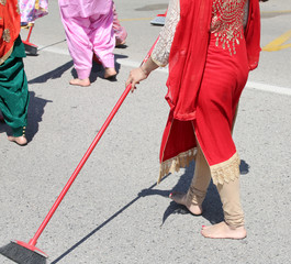 Sikh woman with a red dress cleans the street with a broom