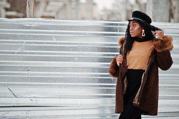 African american woman in sheepskin coat and cap posed at winter day against snowy background.