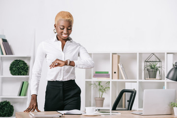 african american businesswoman with short hair looking at watch in modern office