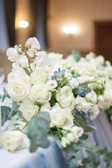 Wedding presidium in restaurant, free space. Wedding banquet table for newlyweds with flowers, greenery, pink cloth and bulbs. Lush floral arrangement on wedding table. Luxury wedding decorations