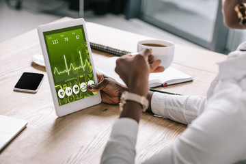 african american woman holding digital tablet with charts and graphs on screen near smartphone