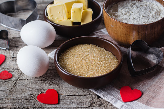 Baking ingredients for Valentine Cookies - flour, sugar, butter, rolling pin, eggs, and heart shape on wooden rustic kitchen table. Cloise-up