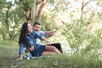 Fototapeta premium young couple sitting on the grass in the forest and looking on sunset, summer nature, bright sunlight, shadows and green leaves, romantic feelings