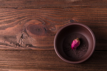 The tea cup and the tea rose bud are on the wooden table.