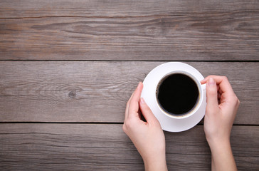 Female hands holding cup of coffee on grey wooden background.