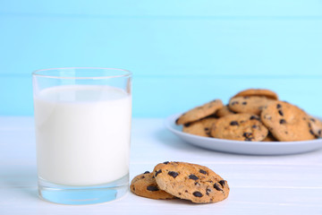 Glass of milk and chocolate cookies on plate on blue background