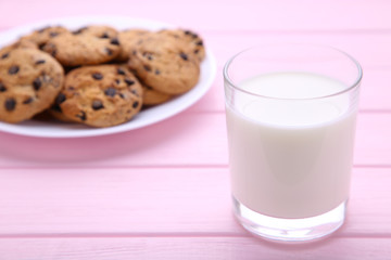 Glass of milk and chocolate cookies on plate on pink background