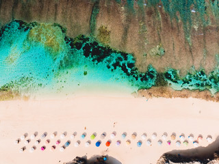 Top view of beautiful sand beach with turquoise ocean water and colorful umbrellas, aerial drone shot