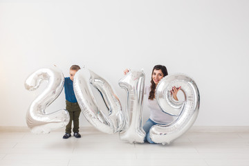 New 2019 Year is coming concept - Mother with her baby son sitting near silver colored numbers indoors.
