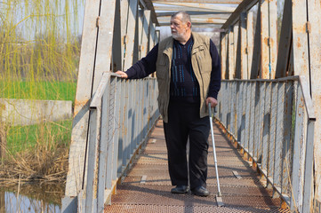 Senior man with walking stick standing on an metal bridge over small river