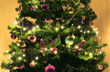 Green Christmas tree with big cones on a beige background. Decorated with bright round balls, garlands and bright lights.