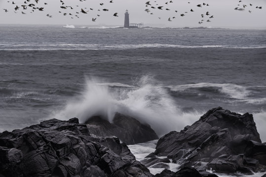 Fototapeta Coast of the Atlantic Ocean. Gloomy weather, waves crashing on the rocks en shore, a lighthouse far into the sea. Black and white photo.  