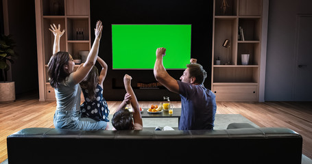 A family is watching a TV and celebrating some joyful moment, sitting on the couch in the living...