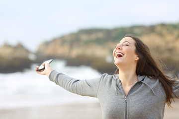 Excited woman holding smart phone on the beach