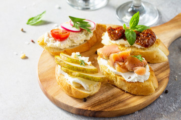 Italian Antipasti snacks set for Wine. Brushetta with Soft Cheese, Pear, Radish, Salmon and Dried Tomatoes on a light stone background.