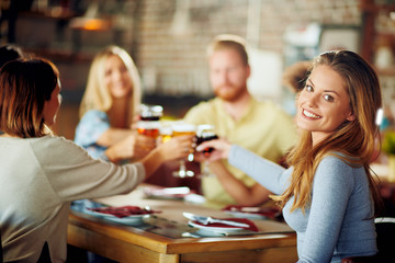 Woman looking at camera and making a toast with glass of wine while sitting in restaurant.