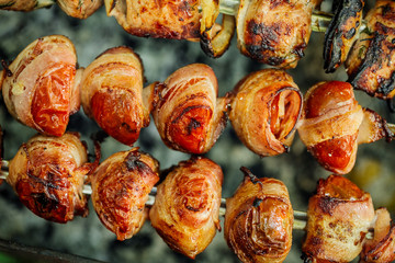 Grilled tomato and bacon skewers in a herb marinade on a grill, top view
