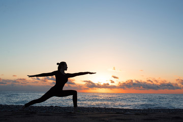 silhouette of woman doing yoga on the beach at sunrise