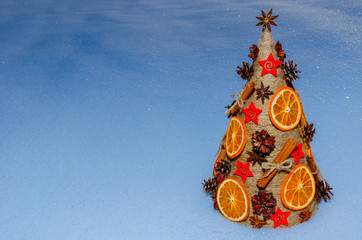  Необычная новогодняя ель, выполненная в стиле «арт-деко» украшенная сушеными апельсинами, сосновыми шишками, бадьяном, корицей и расположенной на снежном покрове. - obrazy, fototapety, plakaty