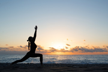 Human silhouette doing yoga on the beach in front of rising sun