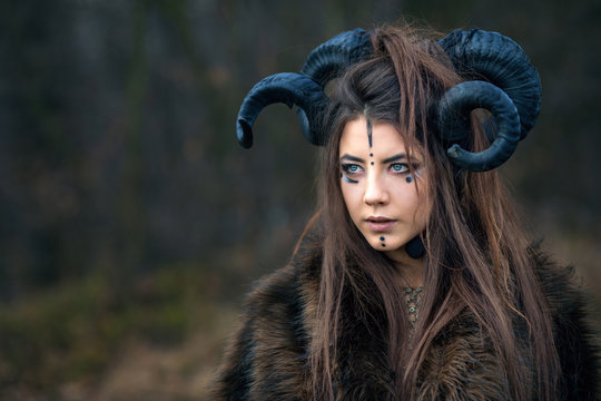 Outdoor portrait of beautiful young woman warrior with blue eyes and specific makeup wearing ram horns and fur collar