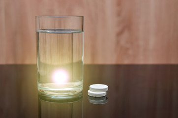 Anesthetic tablet, vitamins, in a glass of water with bubbles on a black table. Copy space. With flare