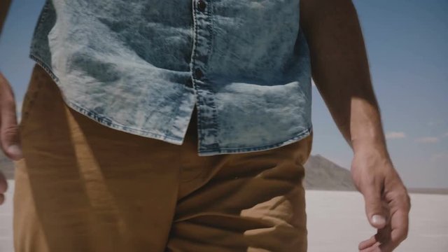Close-up camera tilts up on man in casual clothes walking along incredible salt lake desert flats in Bonneville Utah.