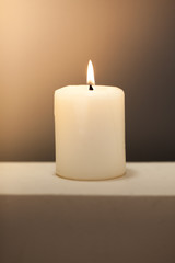 Large lighted candle on a shade contrast background.