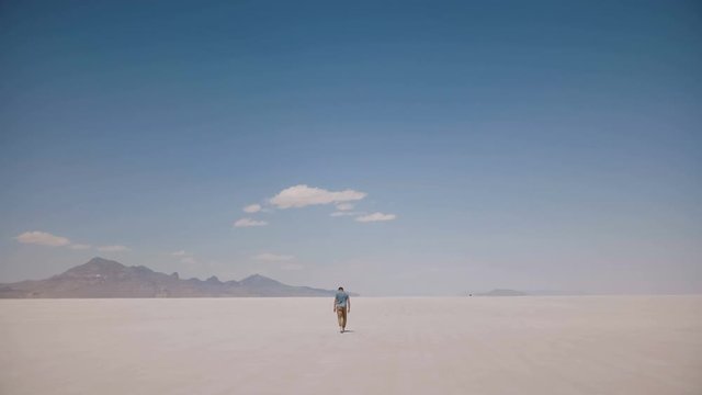 Camera follows tired exhausted young man lost alone walking at dangerous epic hot sunny salt desert lake in Utah USA.