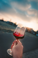 Point-of-View-Shot of a hand holding a glass of red wine into the sun