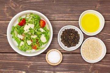 Adding ingredients step. recipe step by step arugula salad in a grey ceramic bowl flatlay on brown wood